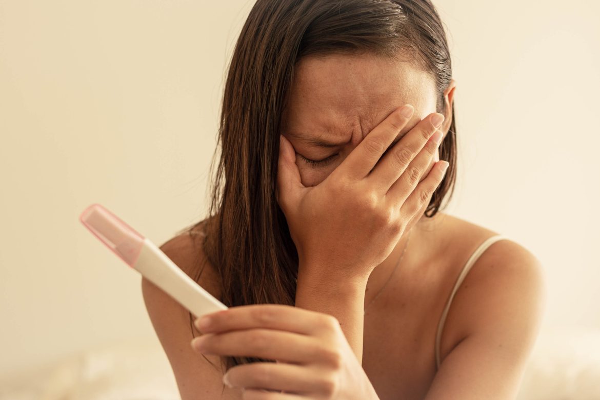 a discouraged woman holding her face and a pregnancy test - how to stay positive when trying to conceive